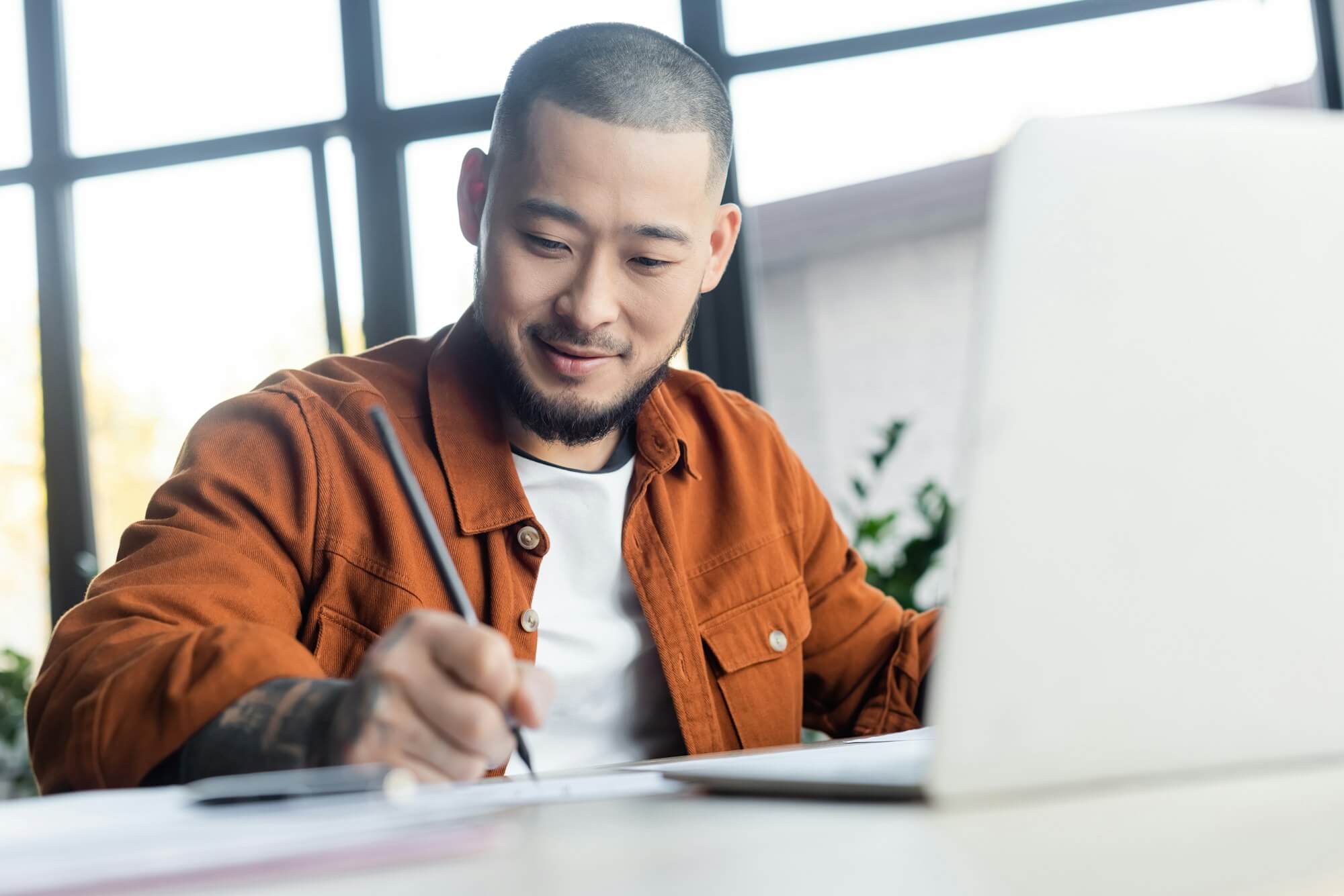 smiling-asian-designer-drawing-near-blurred-laptop-in-architectural-bureau.jpg